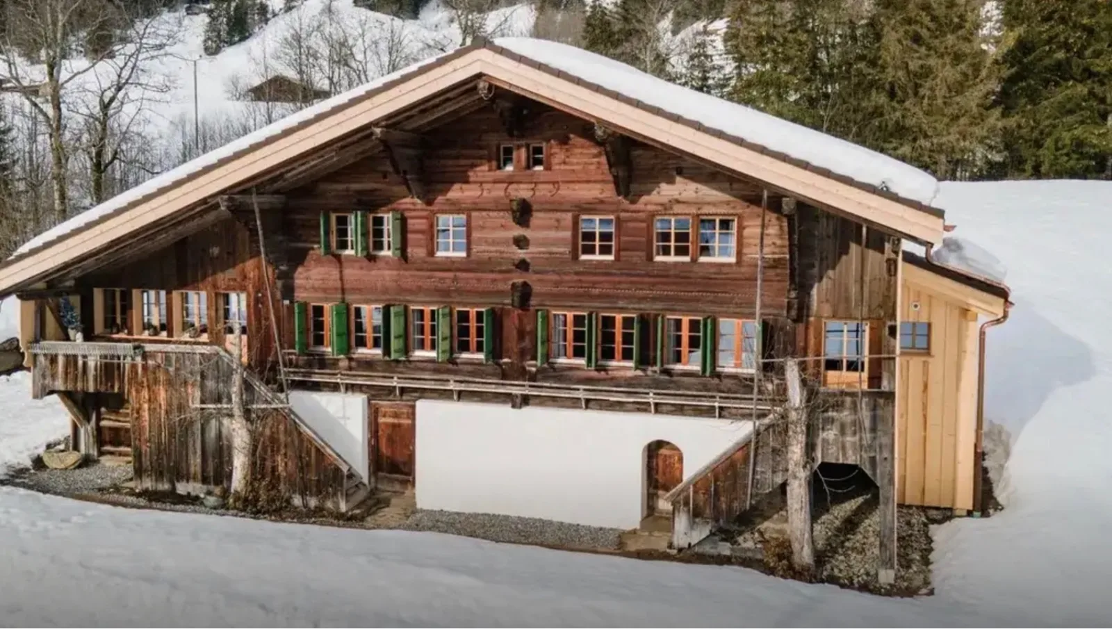 A traditional chalet in winter, its wide gable sheltering rows of shuttered windows